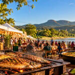 Cena ilustrativa da Festa do Peixe de Camisão 2026 com barracas, pratos de peixe e ambiente de rio e serra